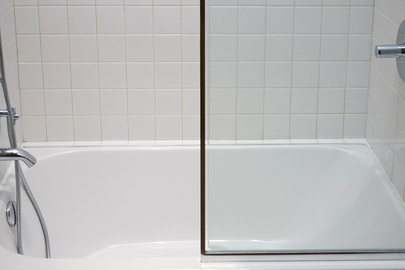 A compact renovated tub and shower combination in a city bathroom: white tub, white stacked rectangular tile surround, polished chrome fixtures, clear glass