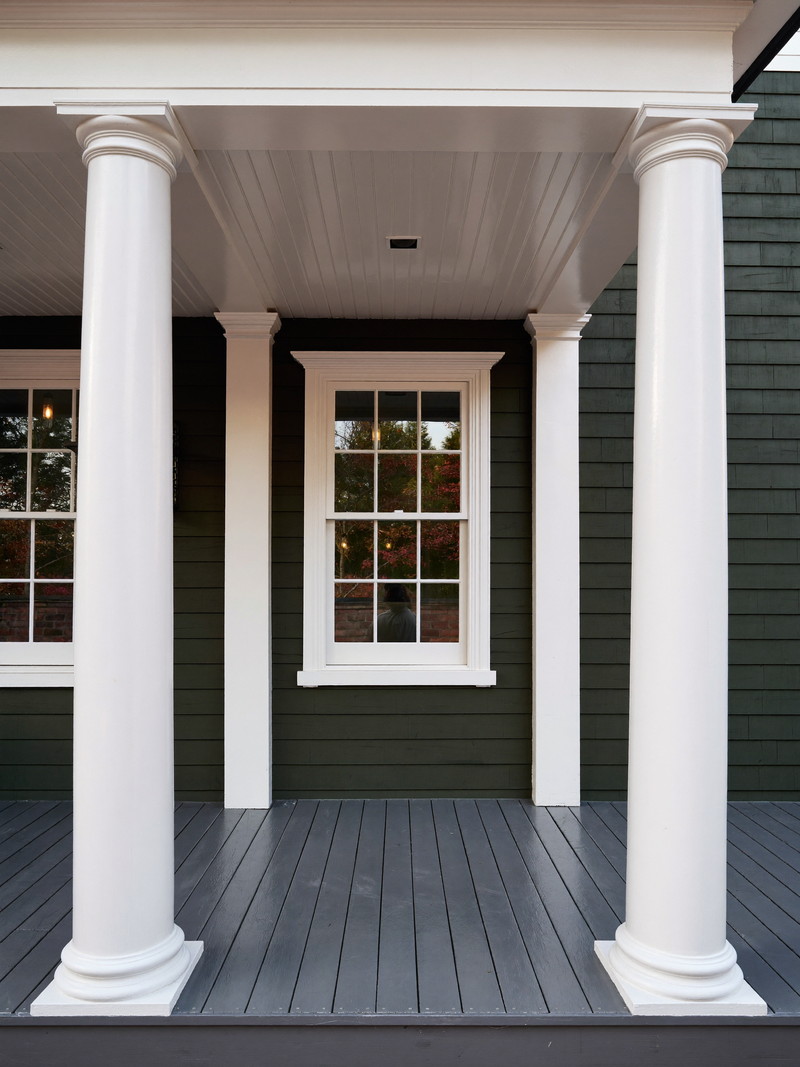 A restored front porch on an older Cambridge home: painted white columns with simple square capitals, gray painted fir floor, white beadboard ceiling, dark