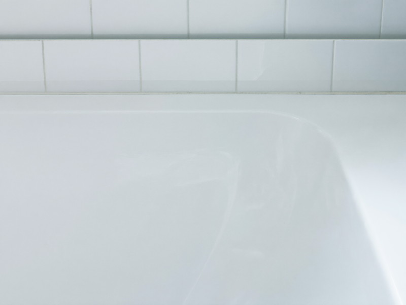 A clean bright white bathtub edge meeting white rectangular wall tile, the joint freshly finished, smooth and tidy, completely bare tub edge, soft daylight
