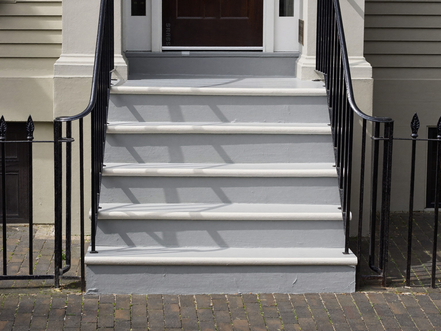 Repaired front entry steps of an older Cambridge home: repainted gray treads, crisp white risers, a simple repainted black iron handrail, brick walk below