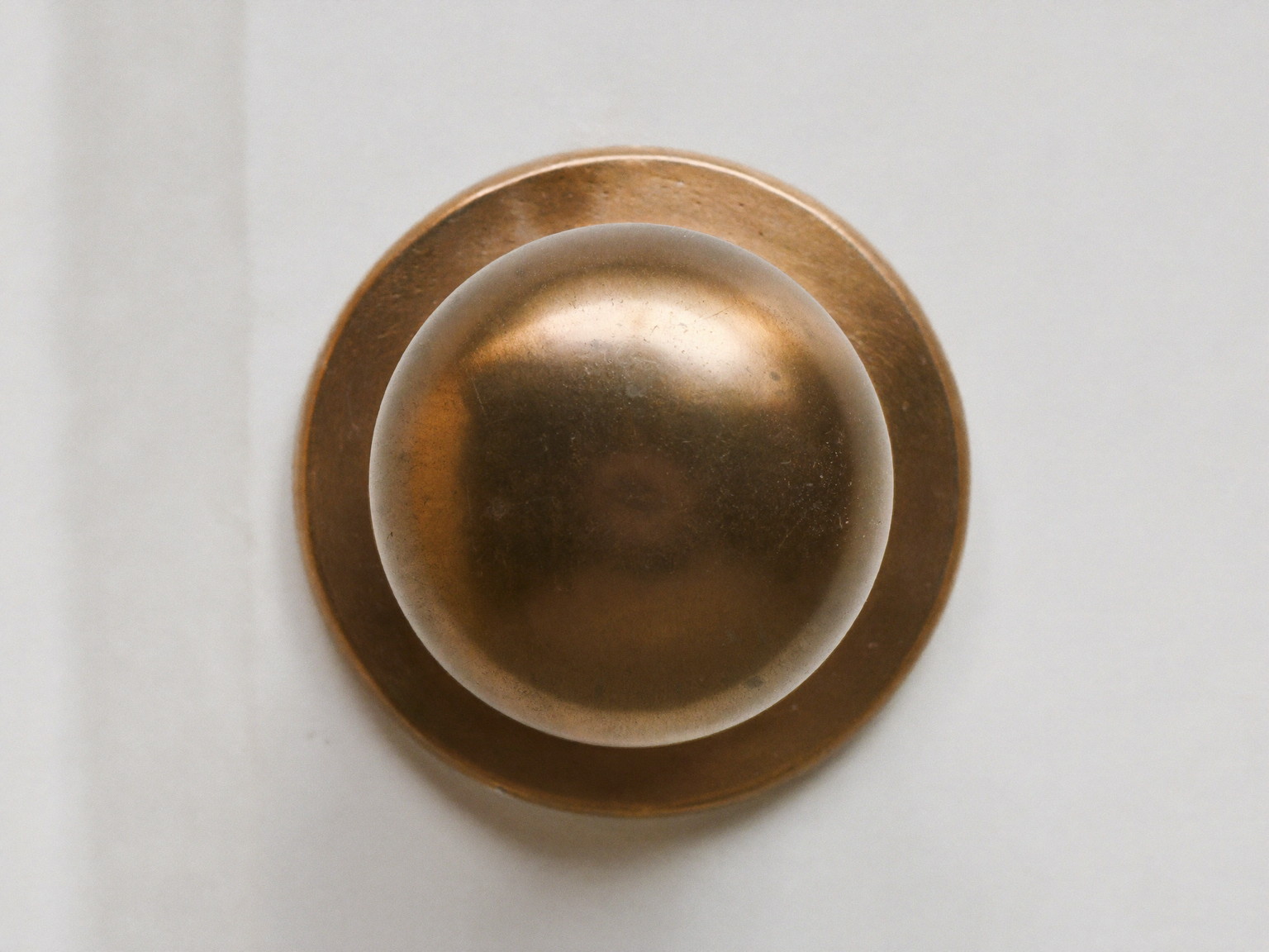 Macro photograph of an aged solid brass door knob with a plain smooth polished dome face and matching plain rosette on a white paneled door, warm patina