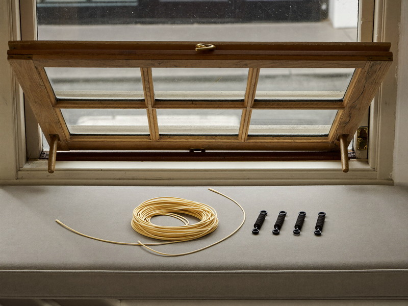 An older double-hung wooden sash window under repair in a city home: sash tilted open on a padded bench, smooth new cotton sash cord coiled neatly beside plain