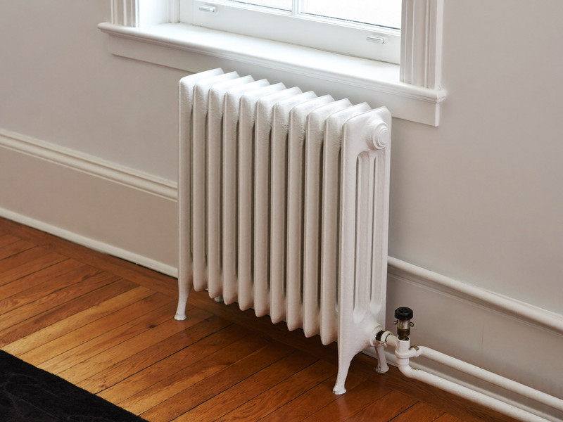 A restored corner of an older Cambridge room: cast iron radiator freshly painted warm white beside refinished honey-toned hardwood floor and bright white