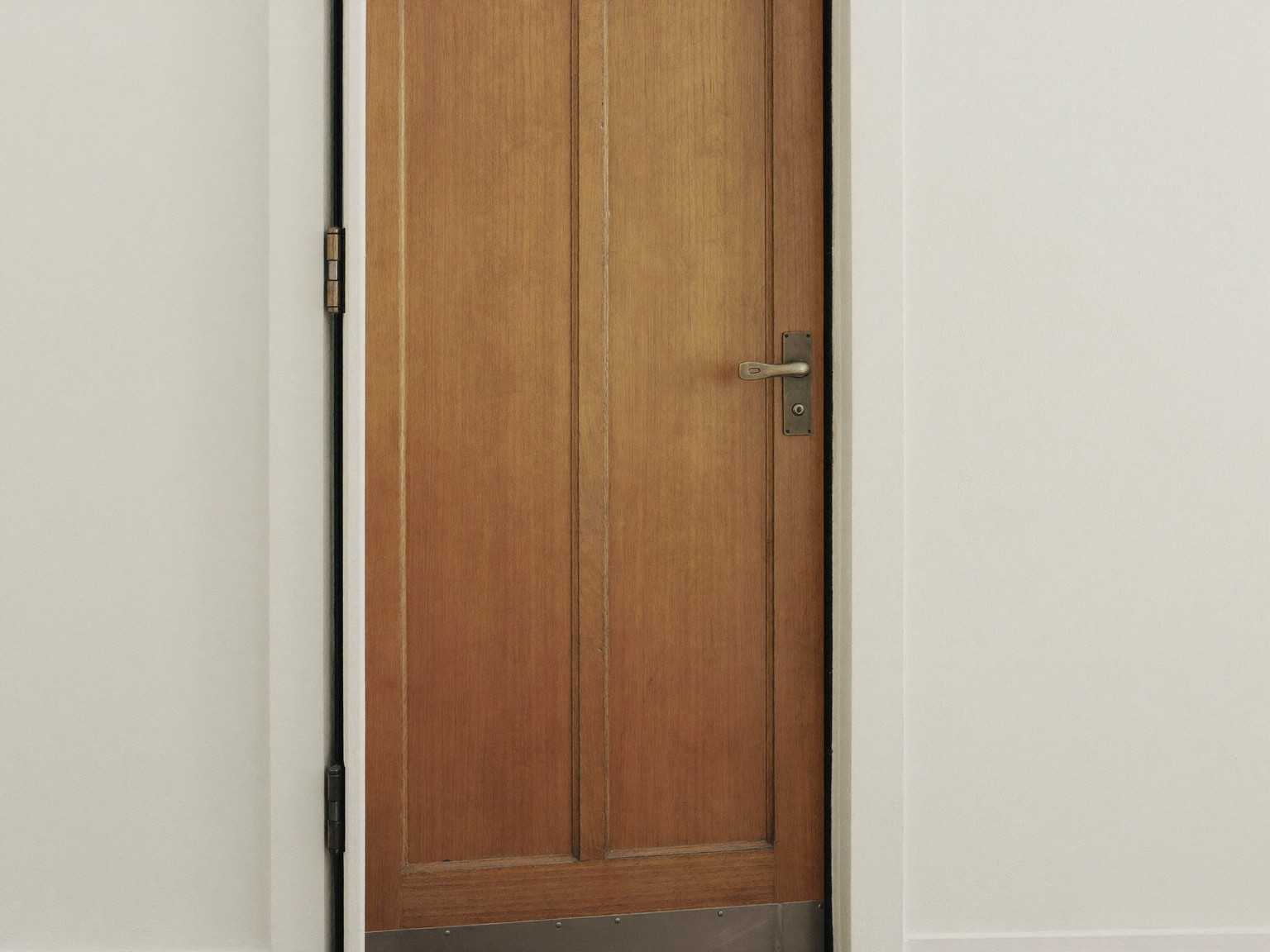 An older wooden door standing in its freshly serviced frame: smooth refreshed painted edge and clean hinges, plain white painted casing, soft daylight