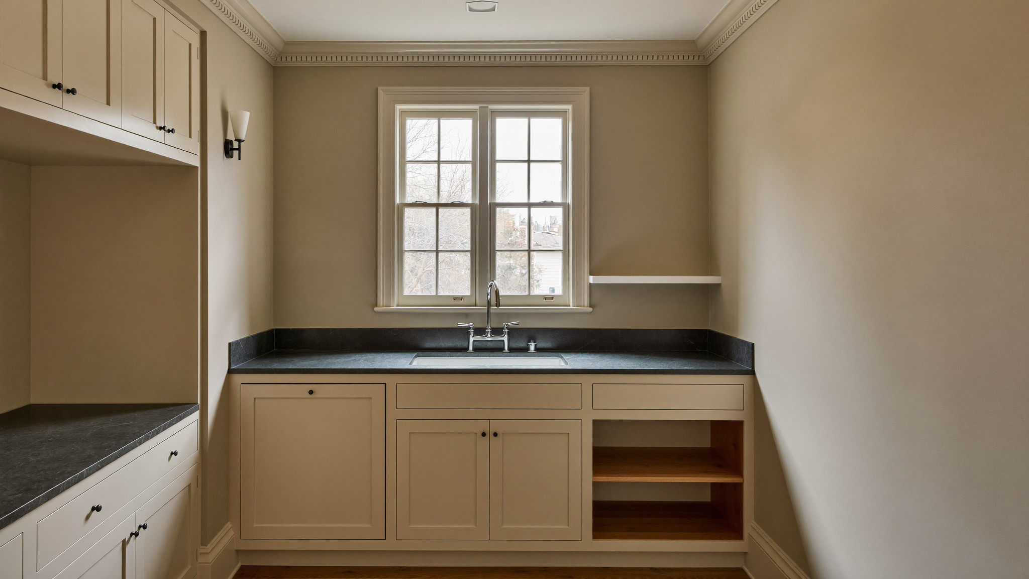 Editorial photograph of a renovated compact galley kitchen in an older Cambridge Massachusetts multifamily home: warm putty-painted inset cabinetry, charcoal