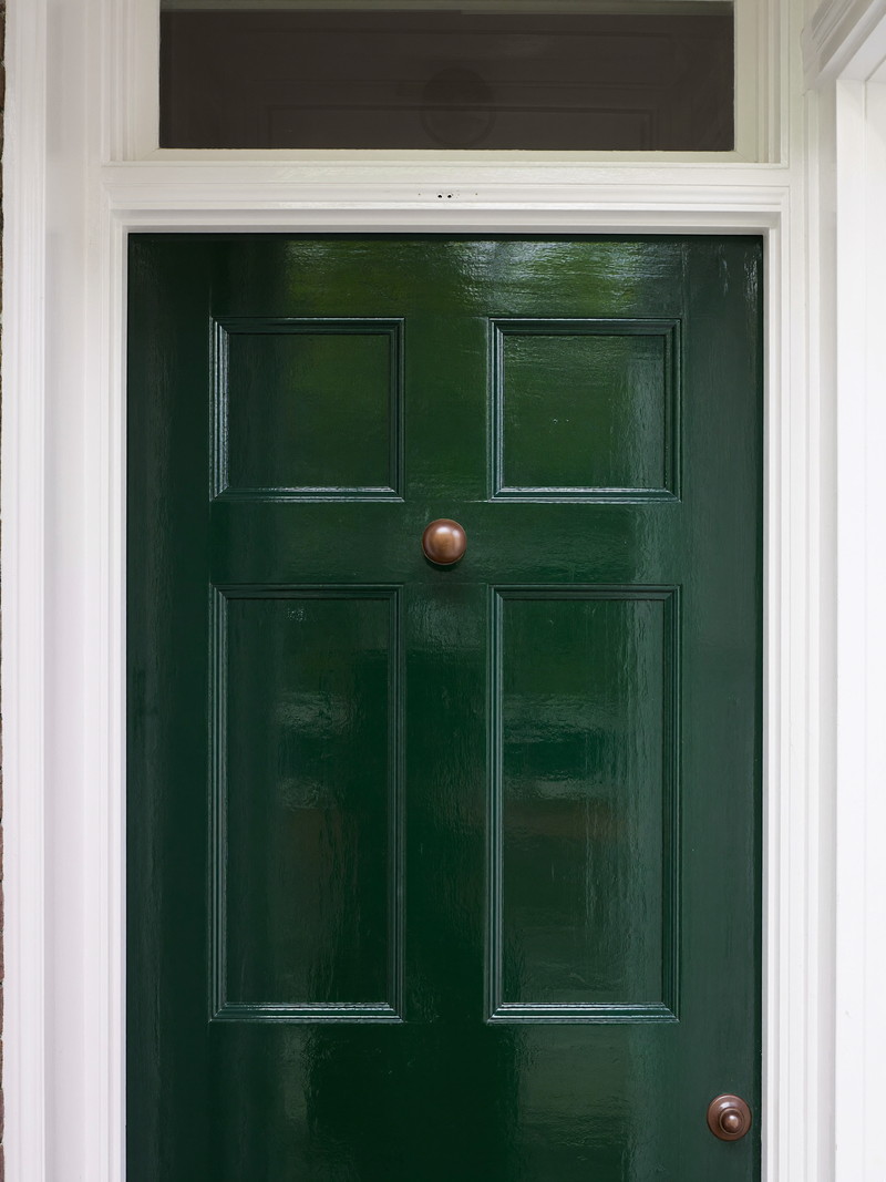 A freshly painted deep green-black front door on an older Cambridge home: glossy smooth finish, plain white painted surround and transom above with clear