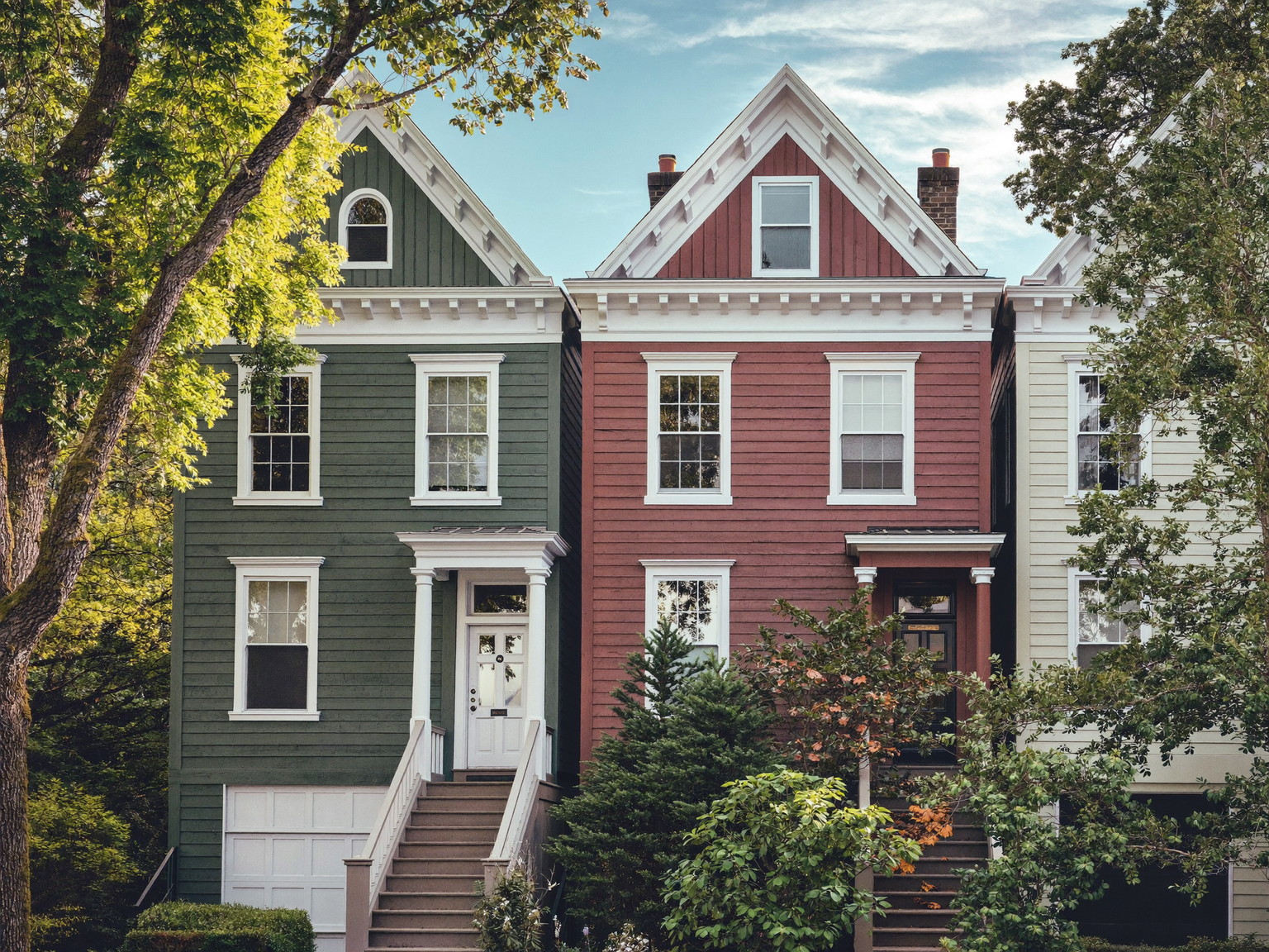 A leafy Cambridge Massachusetts street of freshly painted wooden triple-deckers and Victorian homes: layered colors of sage, putty, and warm white with crisp