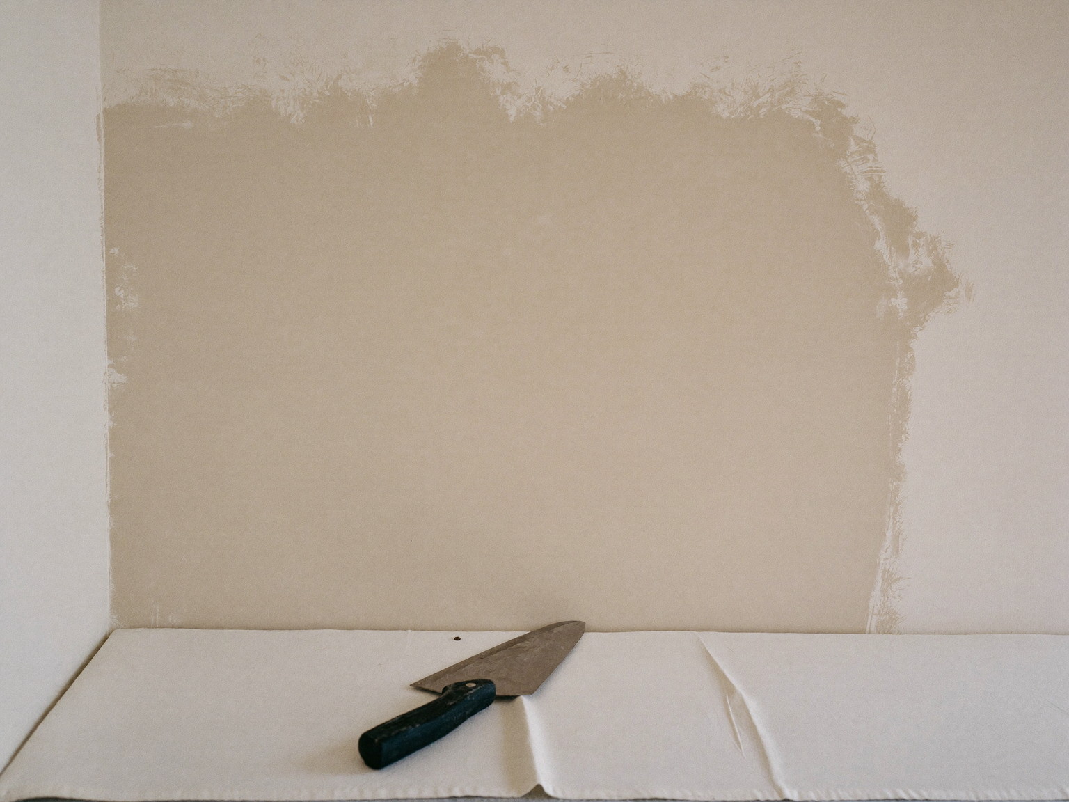 Plaster restoration in progress in an older city home: a wall section skim-coated smooth and drying in soft light, a clean wide unmarked finishing knife