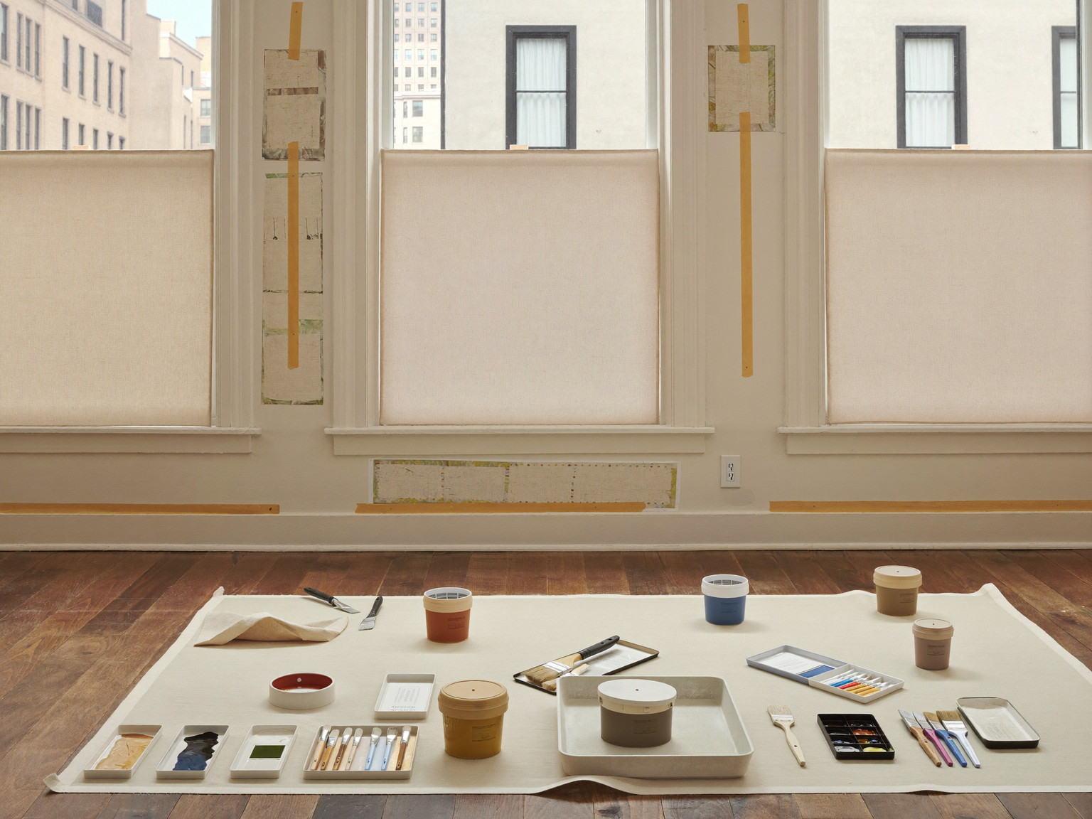 Careful interior painting preparation in an older city home: clean canvas drop cloths over hardwood, tall window casings masked with plain tape, patched