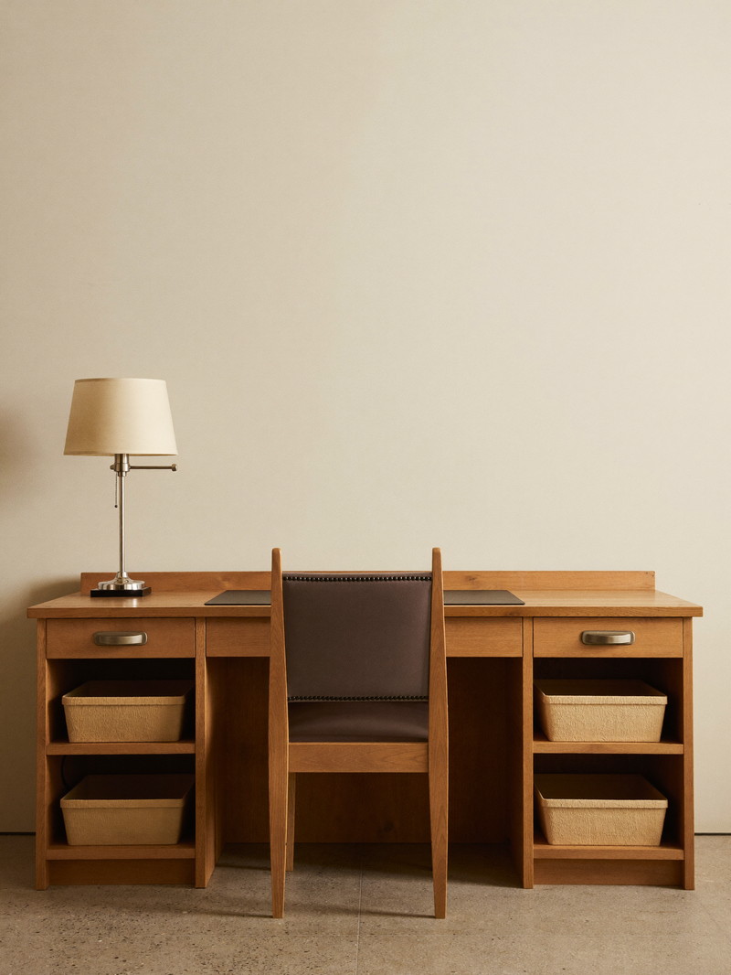 A quiet finished study in a Framingham lower level: built-in hickory desk with plain drawer faces against a smooth bare cream wall, simple upholstered chair