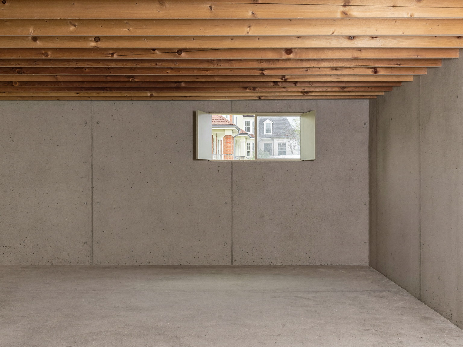 An empty, broom-clean unfinished basement beneath an established suburban colonial, before renovation: a low ceiling with exposed joists overhead