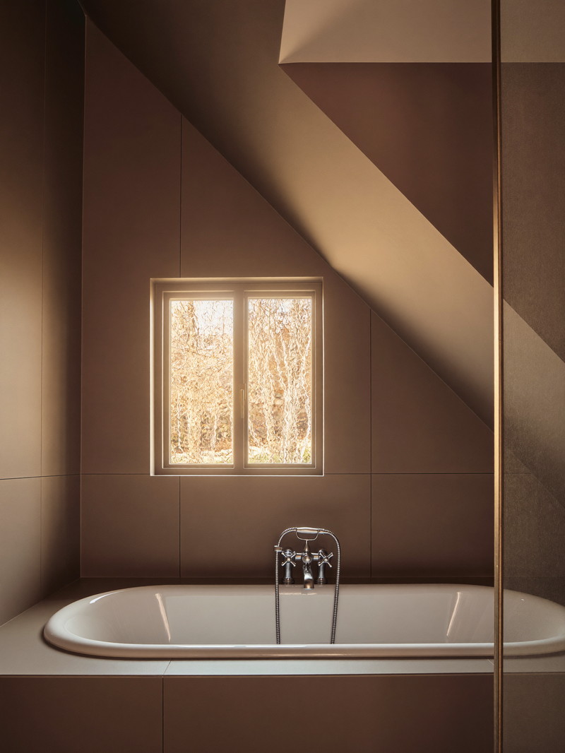 A renovated bathroom under the sloped ceiling of a Framingham cape: white tub with a completely bare rim, warm taupe paneling, satin nickel fixtures