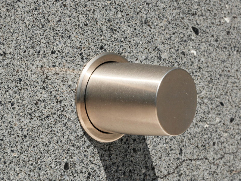 Macro photograph of honed speckled gray granite meeting the plain rounded base of a satin nickel faucet seen from the side