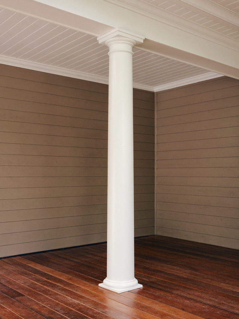 A restored porch corner on an established Framingham colonial: one crisp white round column on warm stained decking, white beadboard ceiling above