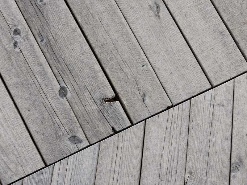 Close-up of old weathered wooden deck boards on an established colonial before rebuilding: silvered gray checked grain, cupped edges and fine cracks
