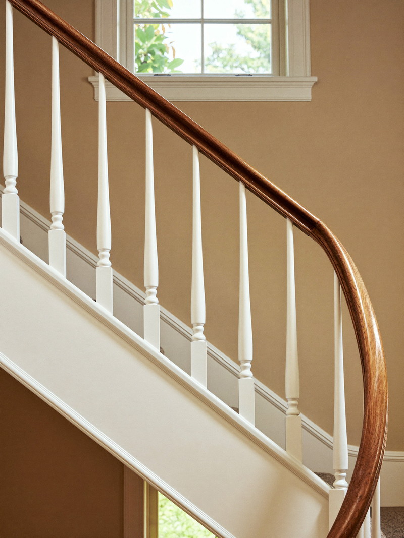 One new baluster among originals: a repaired stair balustrade in an established Framingham stairwell, crisp white spindles beneath a refinished hickory handrail