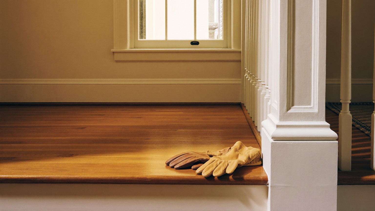 A quiet work moment in the front hall of an established Framingham Massachusetts colonial: completely plain bare tan leather work gloves resting on the hickory bottom sta