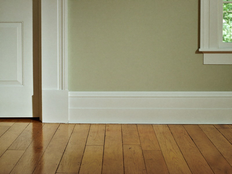 In an established Framingham room, crisp white baseboard and door casing meet a refinished hickory floor: freshly painted warm greige wall above, window light
