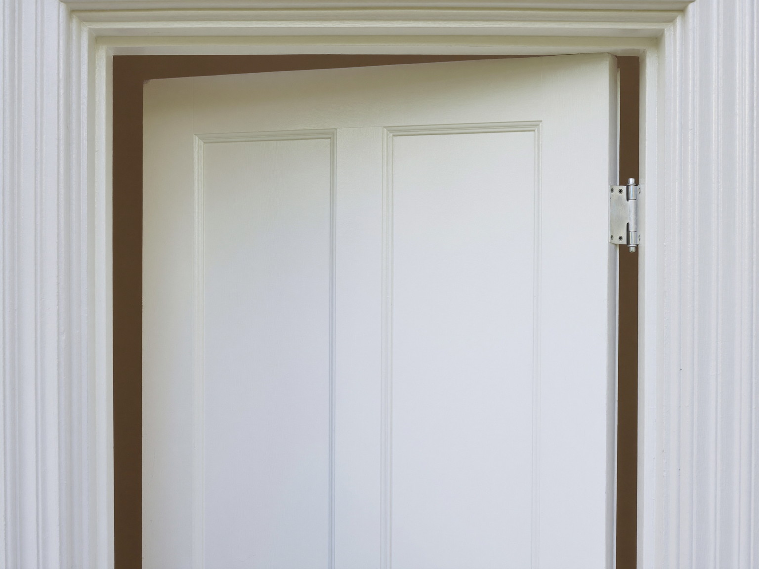 Inside a Framingham colonial entry, a white painted front door stands slightly open in its freshly serviced frame: raised panels visible, smooth refreshed edge