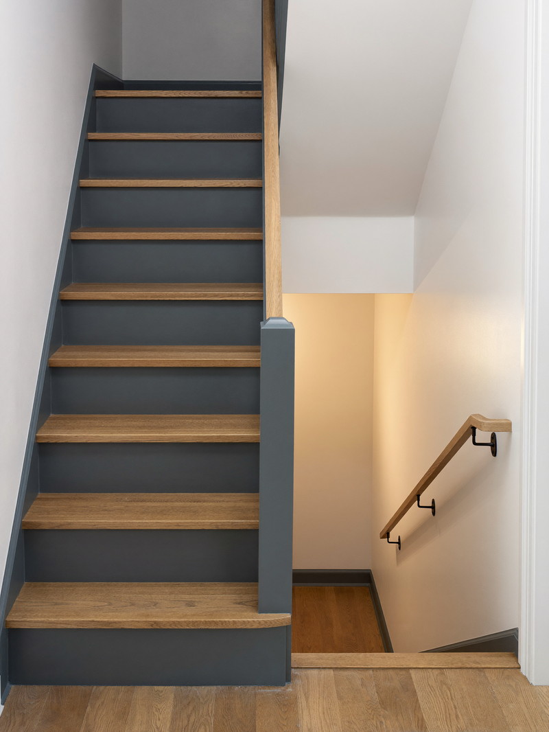 Oak stair with slate-blue risers leading down to a softly lit finished lower level