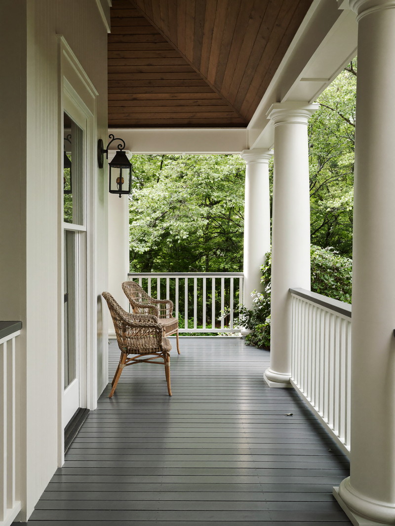 White farmer&rsquo;s porch with round columns, sky-blue beadboard ceiling, rocking chairs, and a stained wood floor