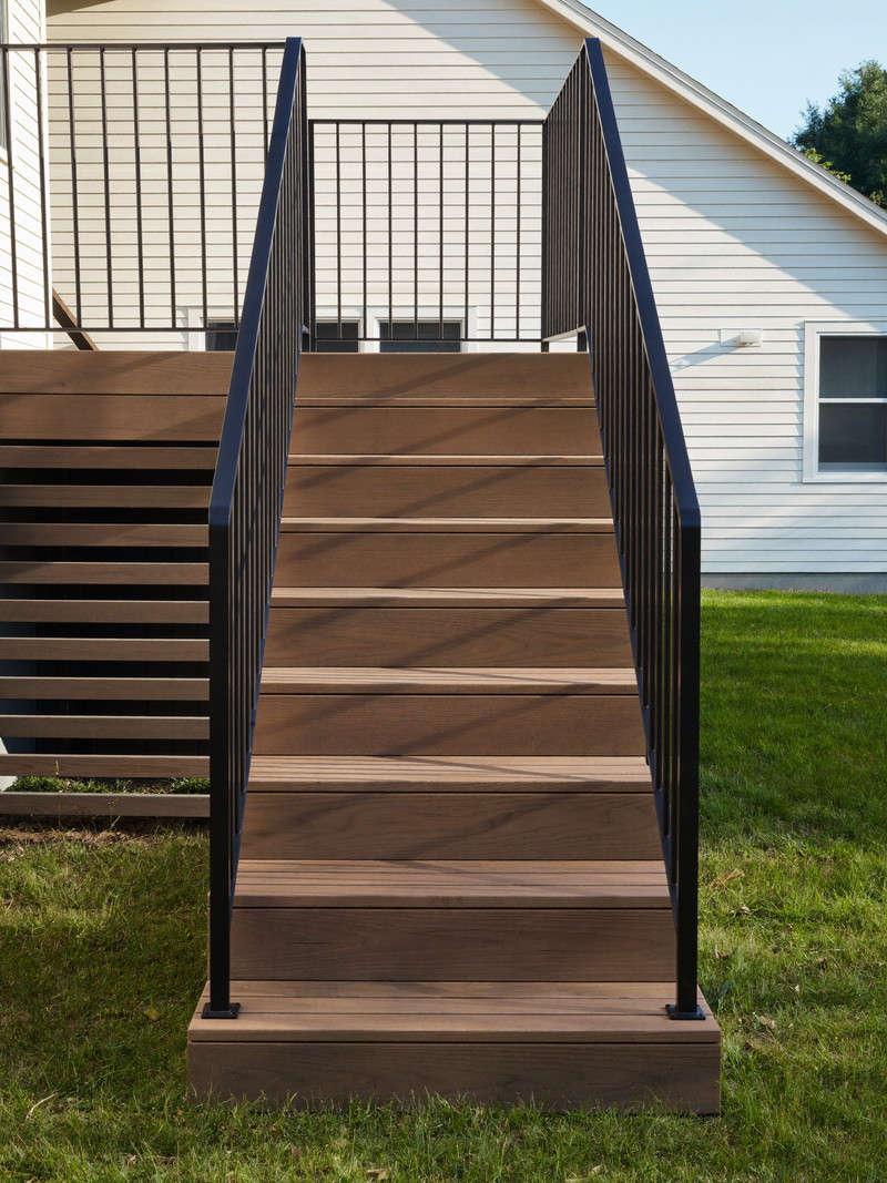 Oak deck stairs with slim black metal balusters and a chamfered cedar newel post in afternoon light