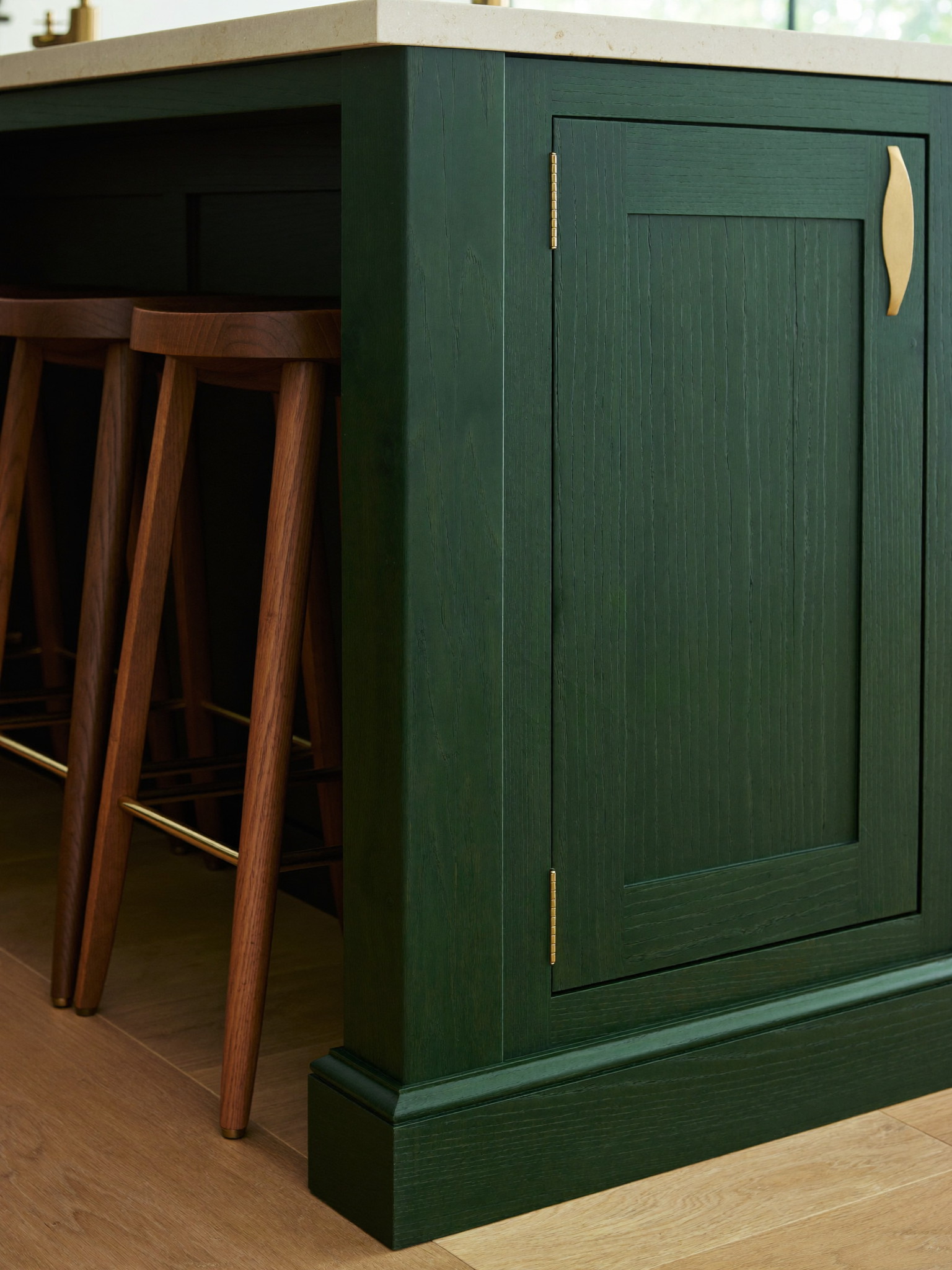 Forest-green island end panel with shaker joinery, brass hardware, and stools tucked under