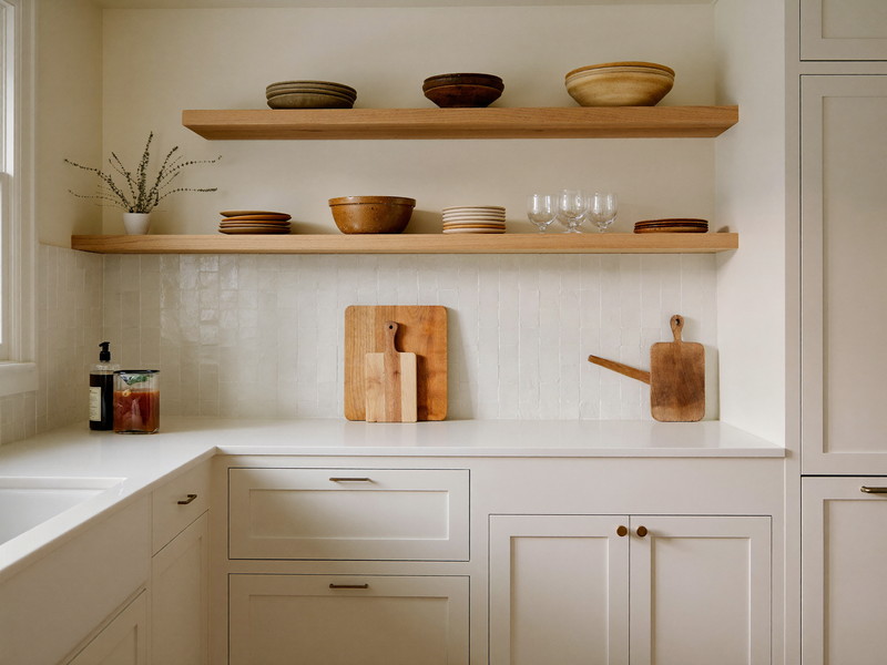 Cream shaker kitchen corner with white counter, handmade tile backsplash, and open oak shelving