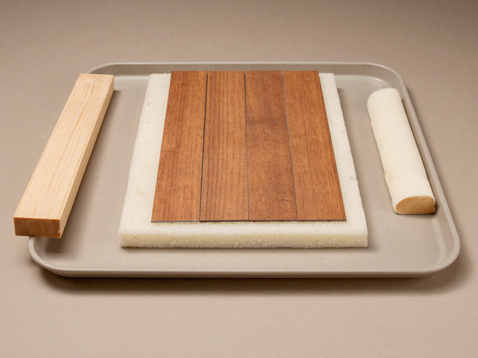 Still life photograph of moisture-smart basement materials on a neutral tray: oak-tone vinyl plank samples, rigid foam insulation corner, plain treated