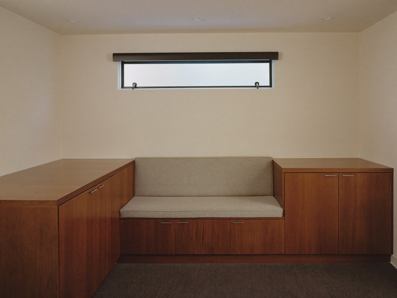 A finished basement family lounge: low built-in bench with plain solid-color cushions along the wall, closed-door walnut storage cabinets with completely