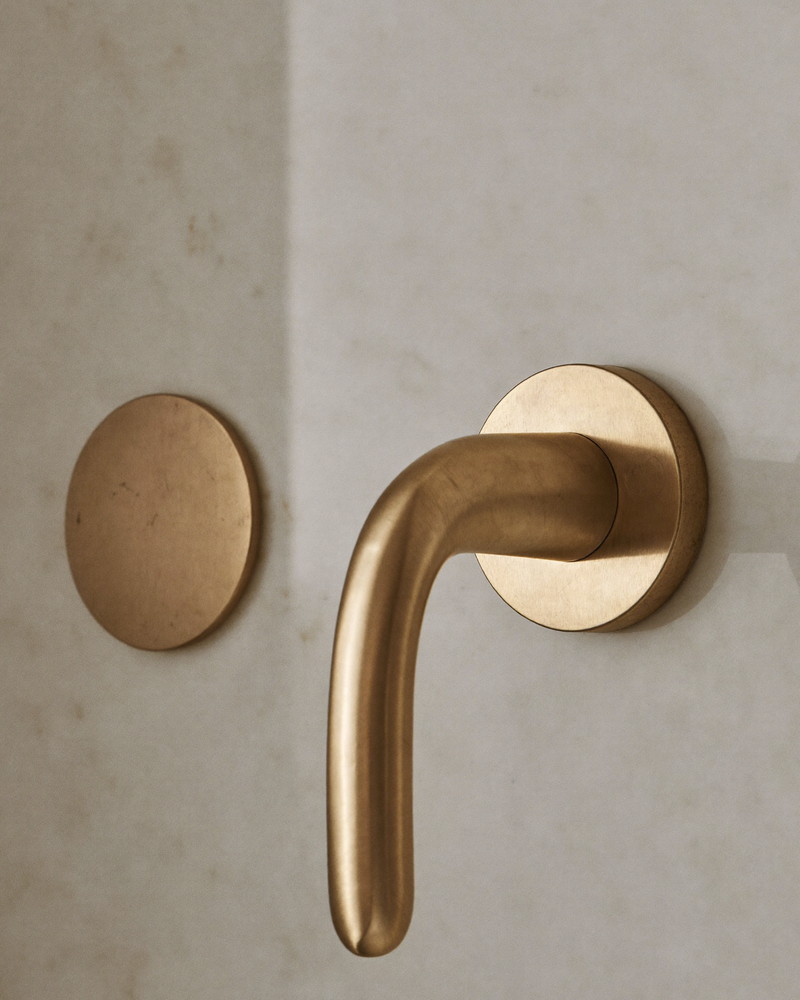 Macro photograph of an unbranded brushed brass bath spout and smooth curved lever handle mounted on honed white quartzite, photographed at a slight angle