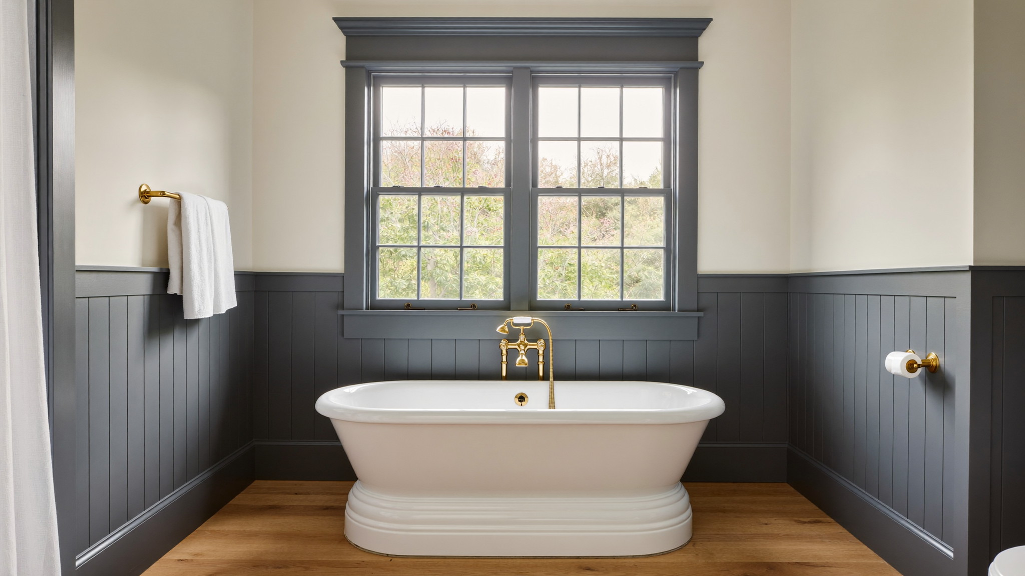 Editorial photograph of a serene renovated bathroom in an established Hopkinton Massachusetts colonial: white freestanding tub beneath a wide double-hung