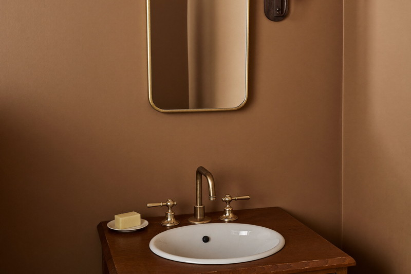 A compact powder room in an established New England colonial: warm putty walls, cherry wood washstand with white top, round brass-framed mirror, plain