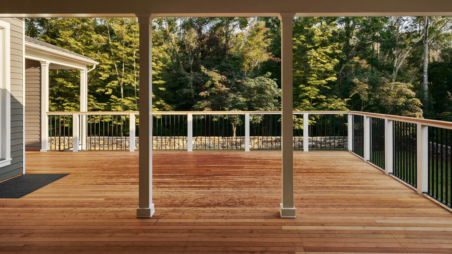 Wide panoramic photograph of a freshly finished cedar deck behind an established New England colonial: warm cedar boards freshly finished, simple white rail