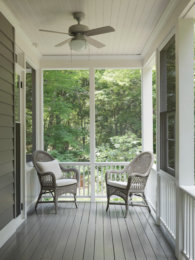 A classic New England screened porch on an established suburban home: gray painted fir floor, white square posts and screen frames, beadboard ceiling with a