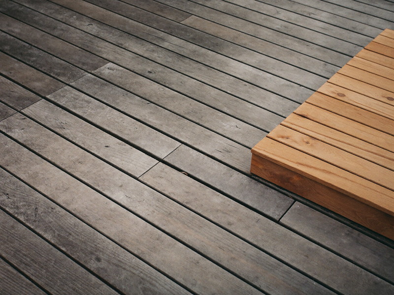 Weathered gray deck boards with soft surface rot beside newly installed warm cedar replacements, honest repair detail on a suburban deck, clean crop, natural