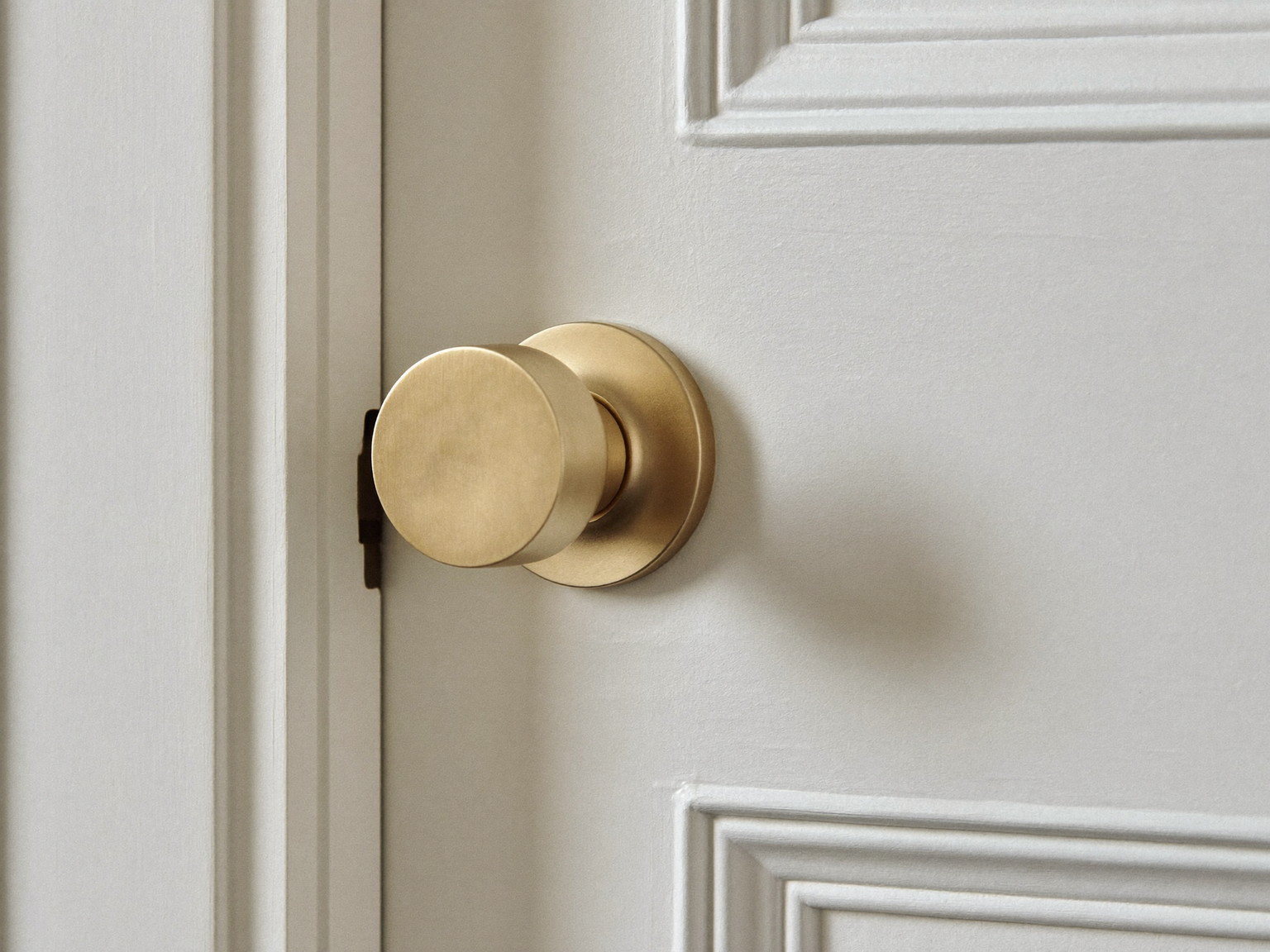 A single plain satin brass door knob and matching rosette installed on a freshly painted white paneled interior door, completely smooth blank unmarked metal