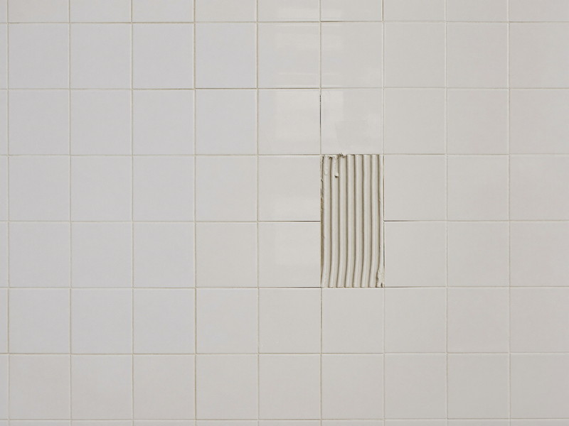 Mid-repair white tile wall in an established home: reset tiles with joints raked clean and ready for fresh grout, continuous sensible joint pattern, clean