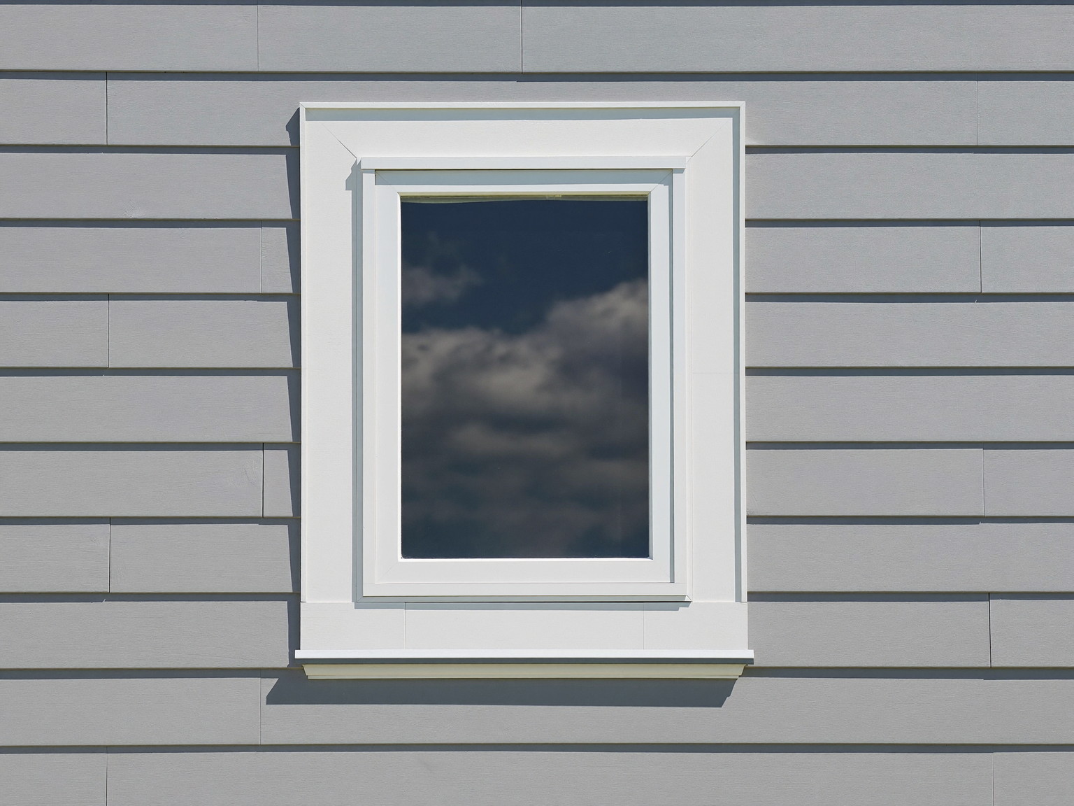 White painted window casing meeting pale gray clapboard siding on an established New England home, crisp freshly painted tight joints, clean straight lines