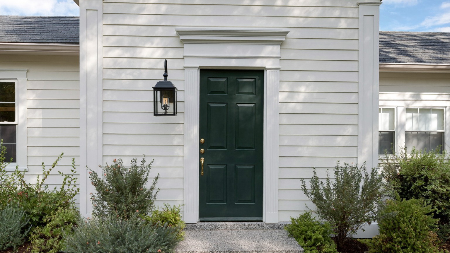 A freshly painted New England colonial entry: crisp white clapboard siding, deep forest-green paneled front door in satin enamel, white casing and dentil