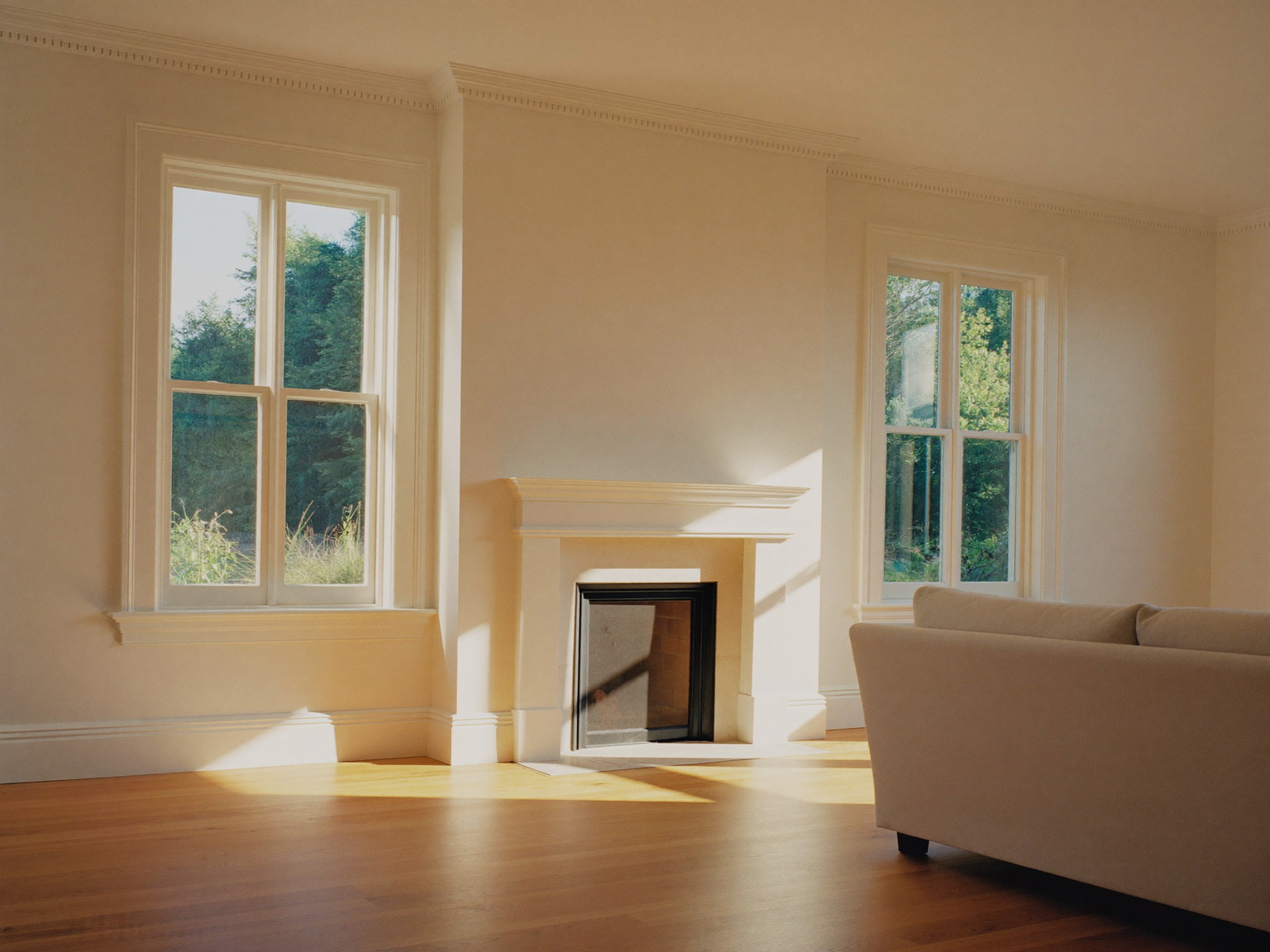 A finished suburban living room with fresh warm-white walls, crisply painted crown molding and window trim, oak floor glowing in afternoon light, simple