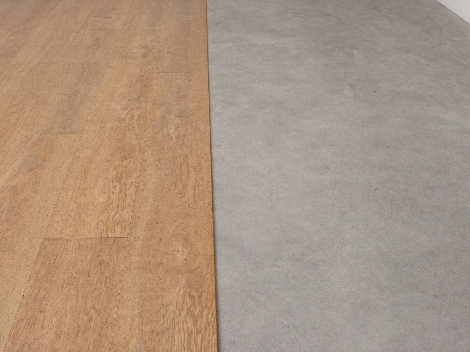 Wide plank maple flooring mid-installation across a clean swept basement floor, the neat transition line showing smooth bare concrete beside finished planks