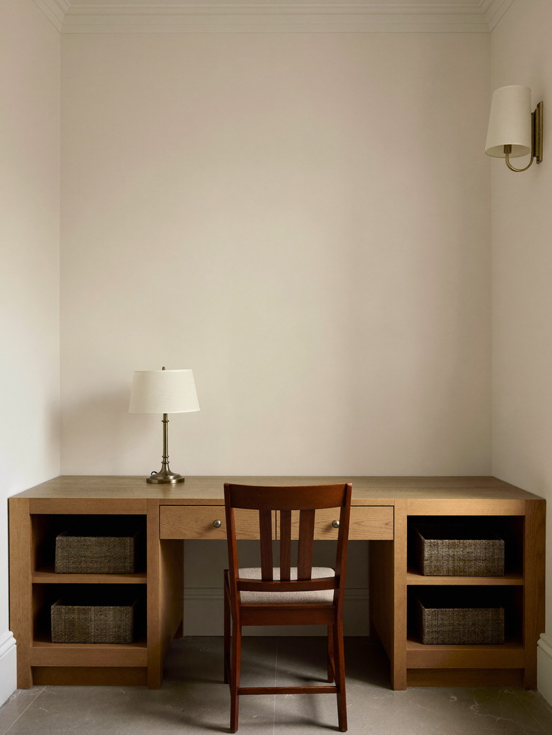 A comfortable lower-level study finished in a renovated colonial basement: built-in maple desk with plain drawer faces against a smooth bare ivory wall