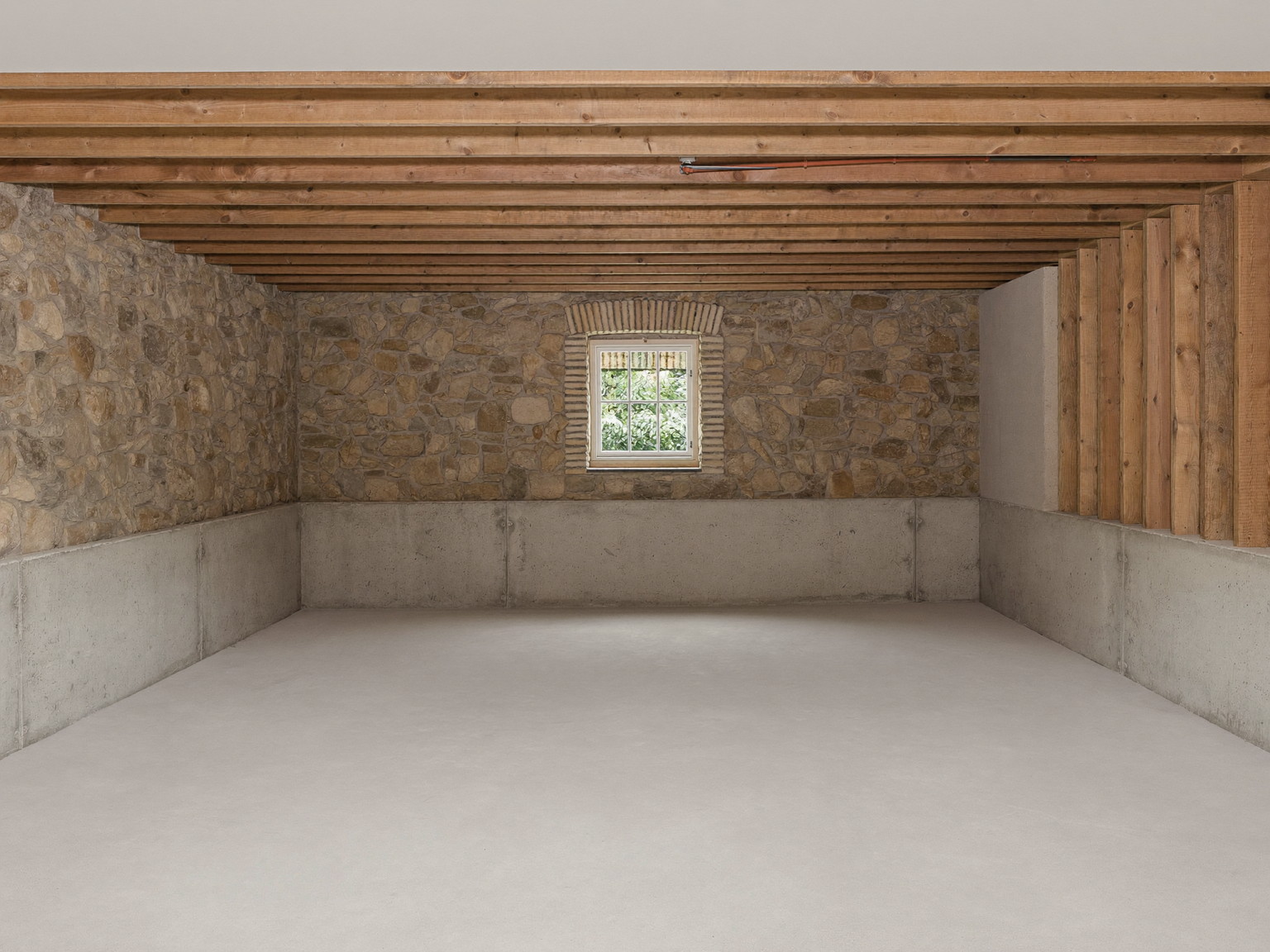 An empty, broom-clean unfinished basement beneath a historic colonial, before renovation: a low ceiling with exposed joists overhead