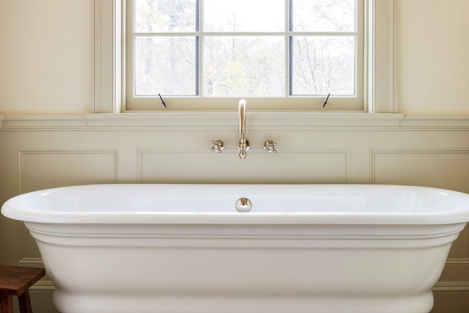 A renovated bathroom in a historic Lexington colonial: white freestanding tub beneath a deep-silled window with muntins, ivory wainscot