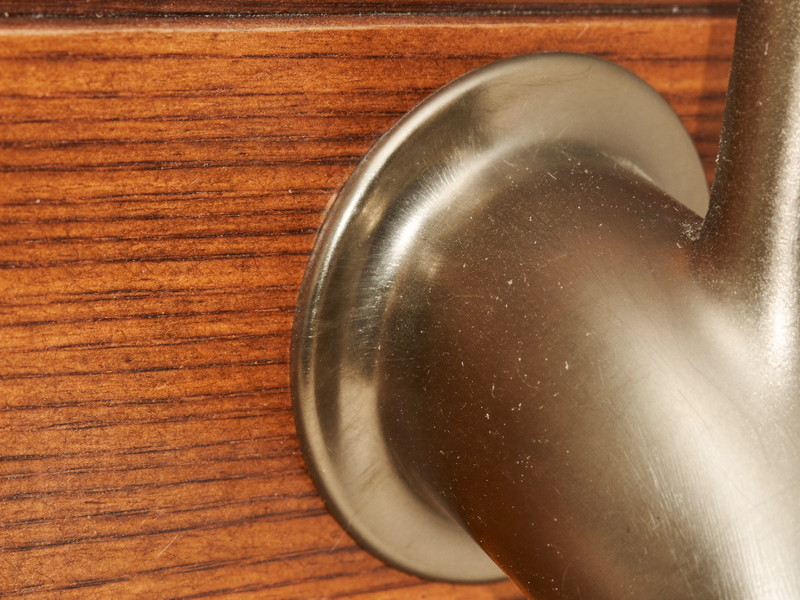 Macro photograph of warm maple wood grain meeting the plain rounded base of a brushed pewter faucet seen from the side