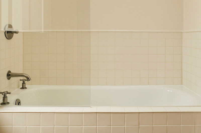 A tidy tub and shower combination in a colonial family bathroom: white tub, ivory square tile surround, brushed pewter fixtures, every ledge and edge completely bare