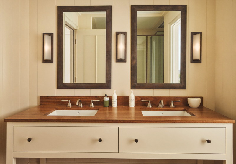 A double ivory vanity with warm maple top under two rectangular pewter-framed mirrors, brushed pewter sconces, ivory walls, comfortable colonial bathroom