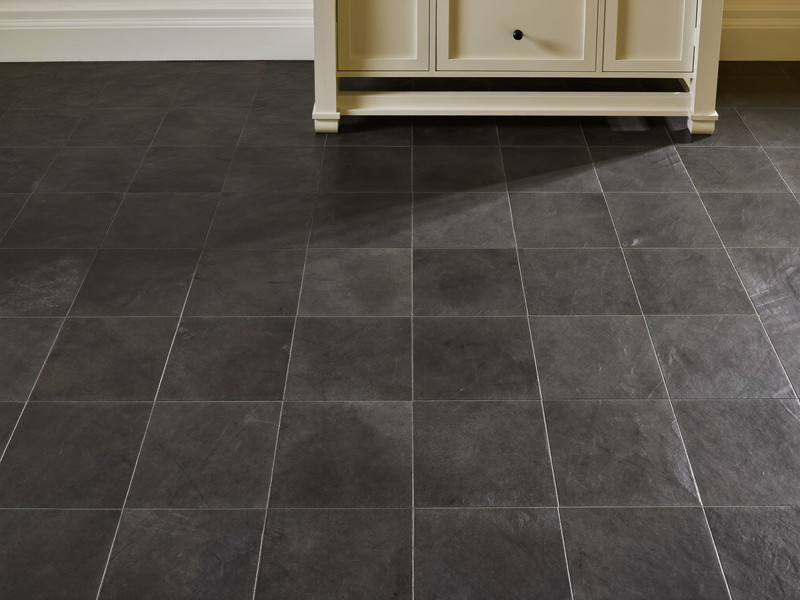 Honed slate-gray floor tile in a renovated colonial bathroom, plain field tile only, every tile flat and even, foot of an ivory vanity visible, natural light