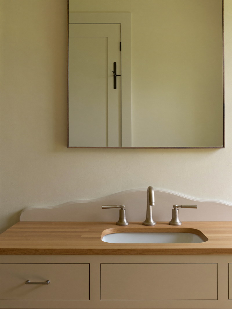 An ivory painted bathroom vanity with a warm maple top and brushed pewter faucet with smooth lever handles, rectangular pewter-framed mirror on an ivory wall